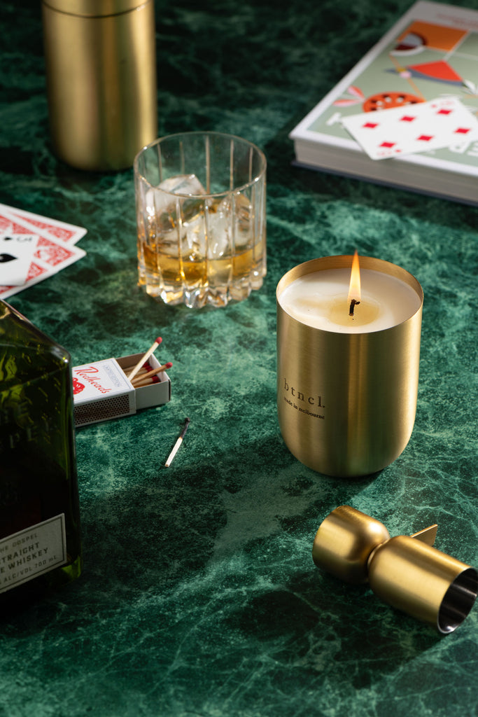 Brass candle on green marble table with playing cards and glass of whiskey
