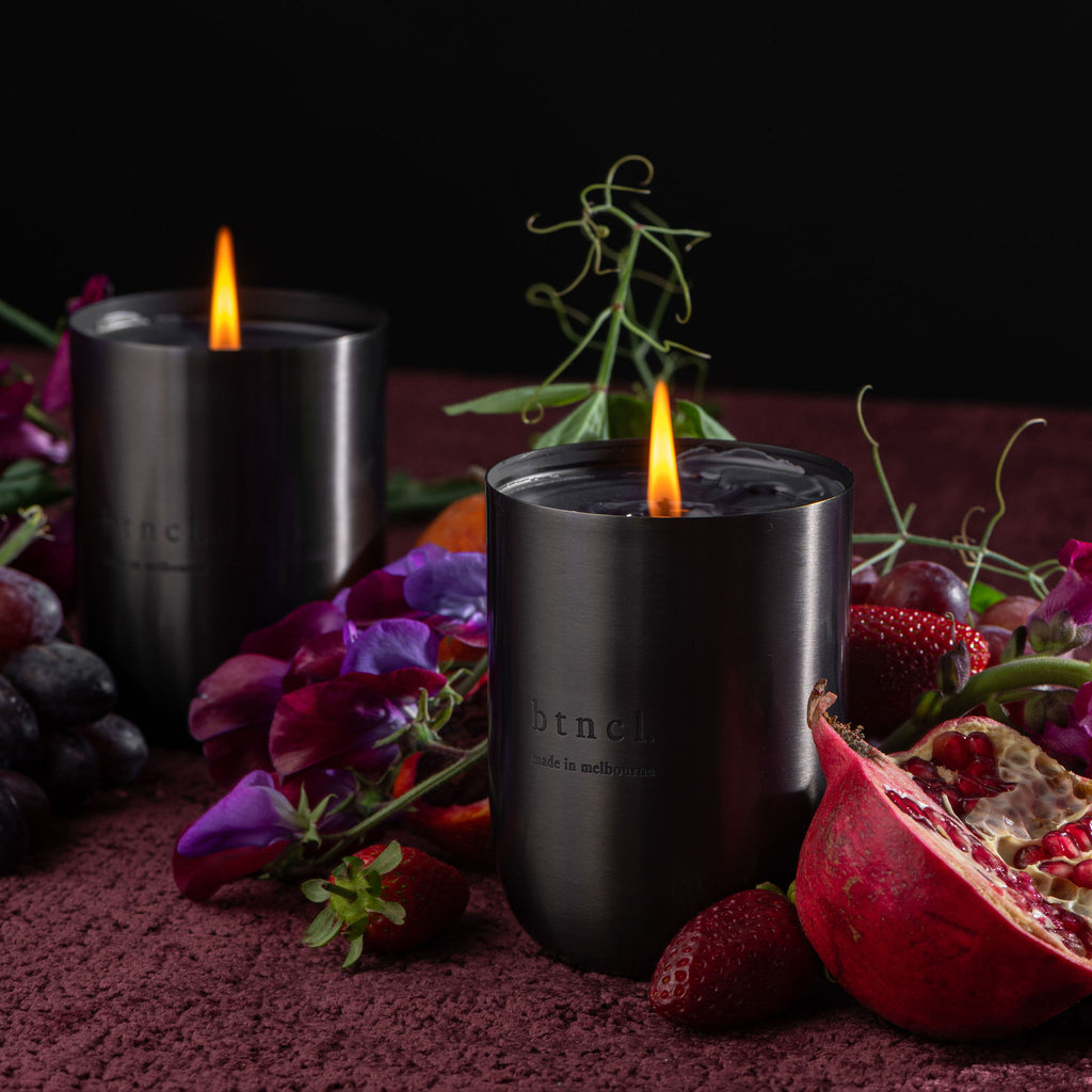 Two black btncl candles with fruits and warm maroon velvet