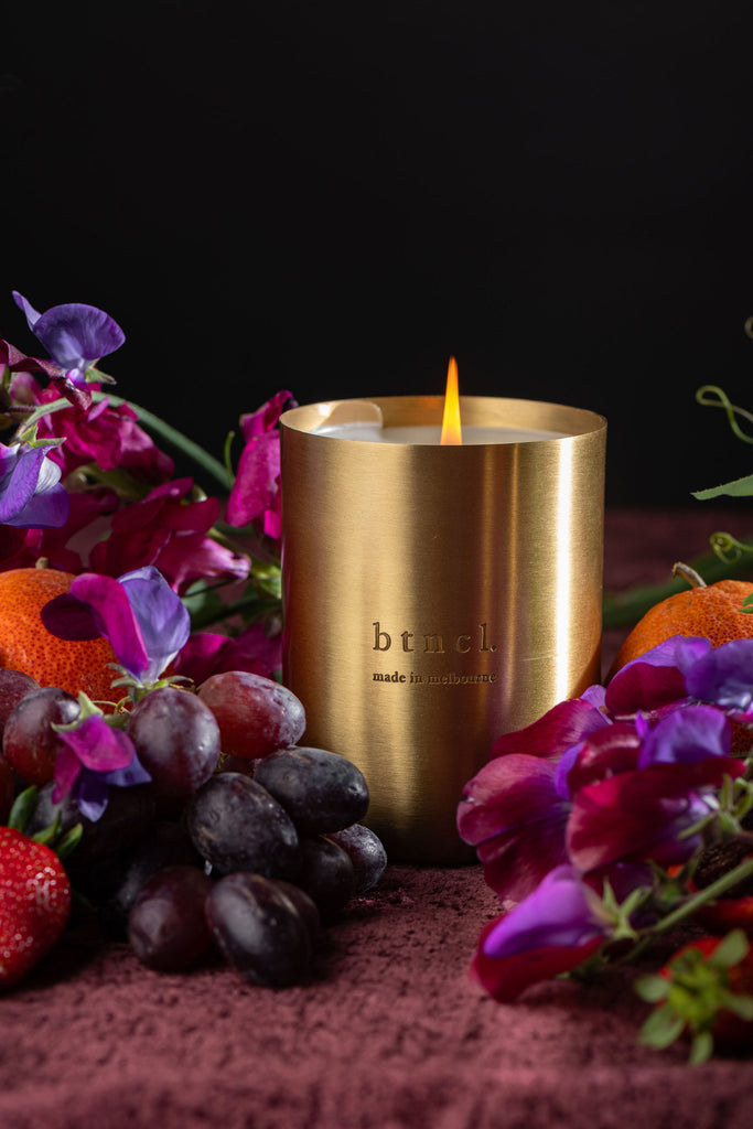 btncl brass candle on dark velvet with fresh florals and grapes