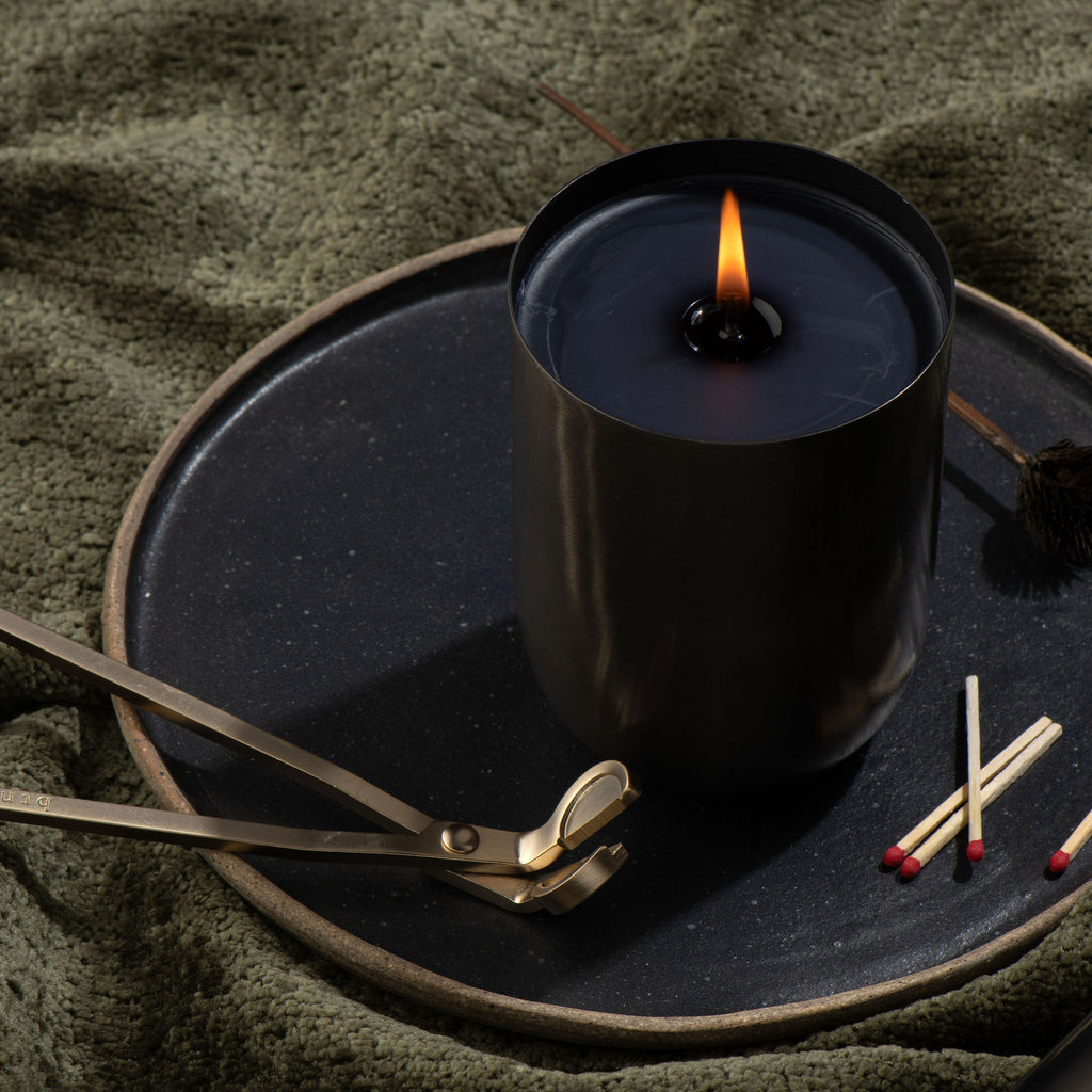 Black candle sitting on dark dish with with trimmer and matches